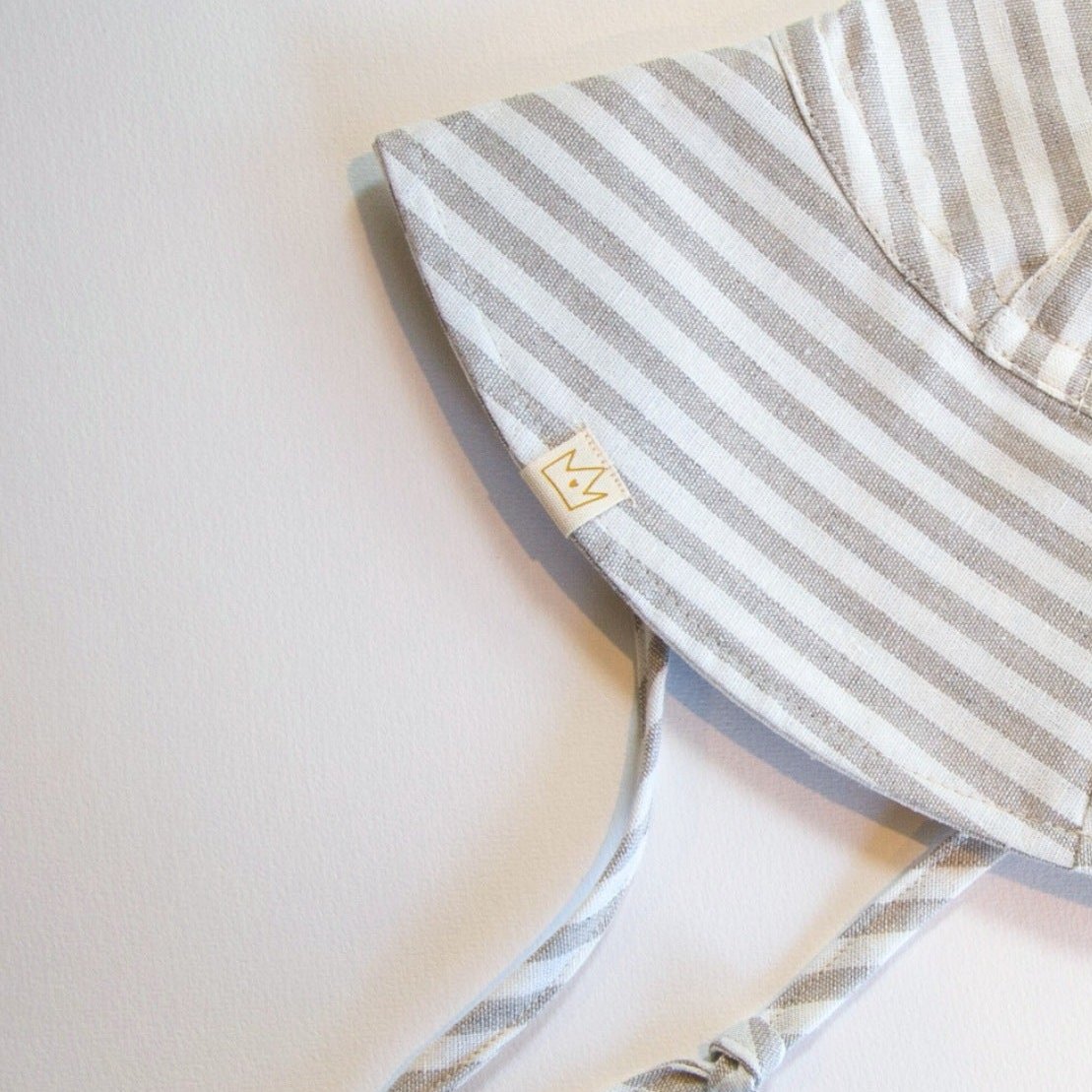 Back view of the Cloudy Stripes grey stripe baby sun hat, featuring the adjustable neck tie for a secure and comfortable fit. The shot also highlights the exterior label tag, showcasing the attention to detail and quality craftsmanship