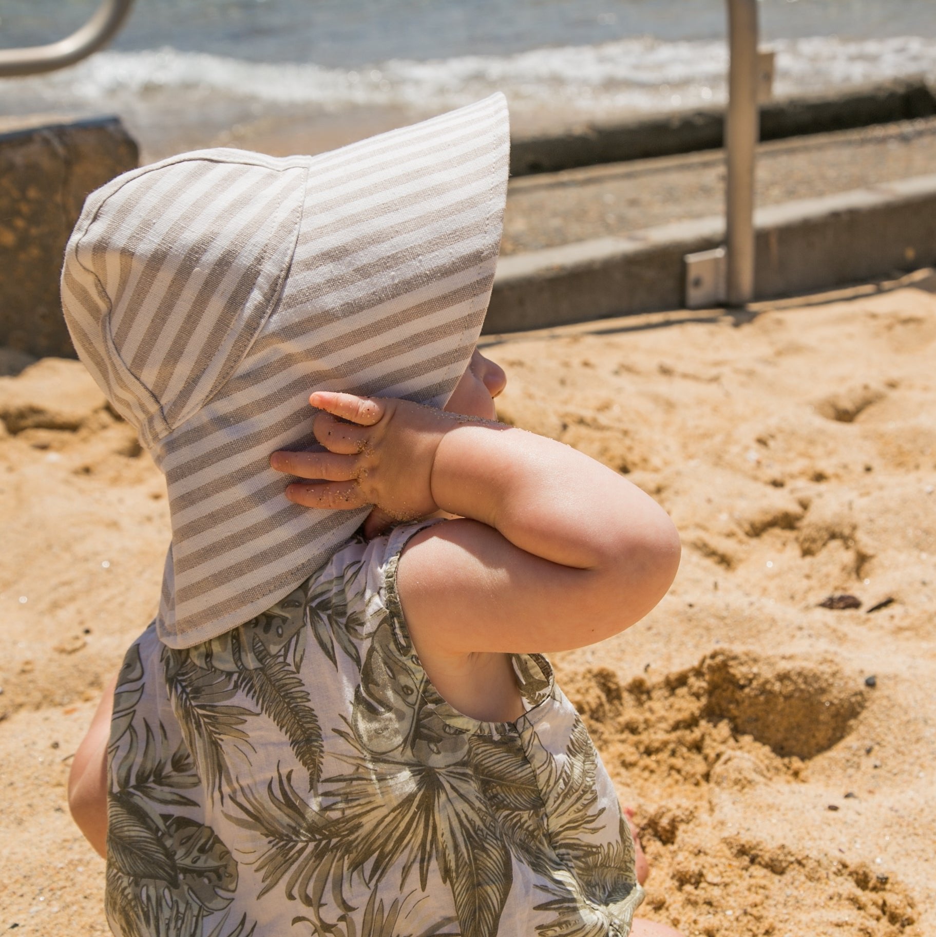 Lifestyle shot of Cloudy Stripes grey stripe baby sun hat, worn by a baby enjoying the outdoors on a sunny day, highlighting its comfort and style