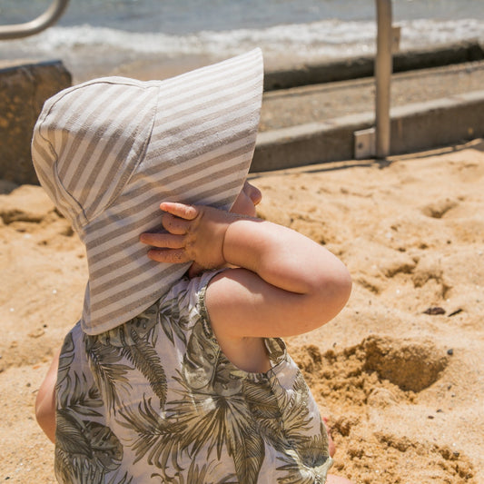 Lifestyle shot of Cloudy Stripes grey stripe baby sun hat, worn by a baby enjoying the outdoors on a sunny day, highlighting its comfort and style
