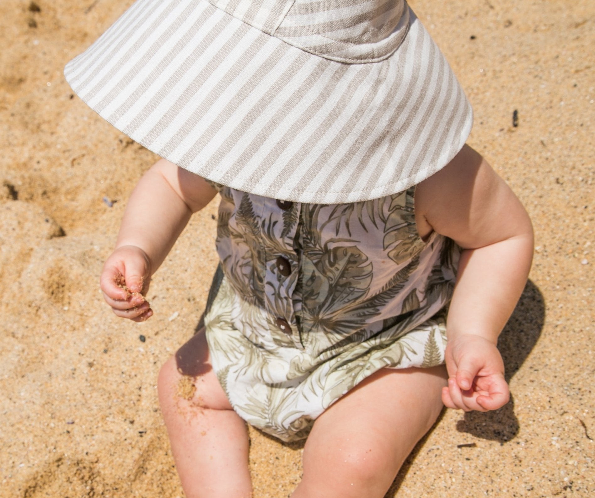 Lifestyle shot of Cloudy Stripes grey stripe baby sun hat, worn by a baby enjoying the outdoors on a sunny day, highlighting its comfort and style
