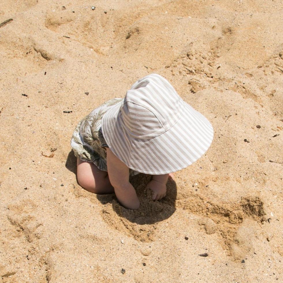 Lifestyle shot of Cloudy Stripes wide brim grey stripe baby sun hat, worn by a baby enjoying the outdoors on a sunny day, highlighting its comfort and style
