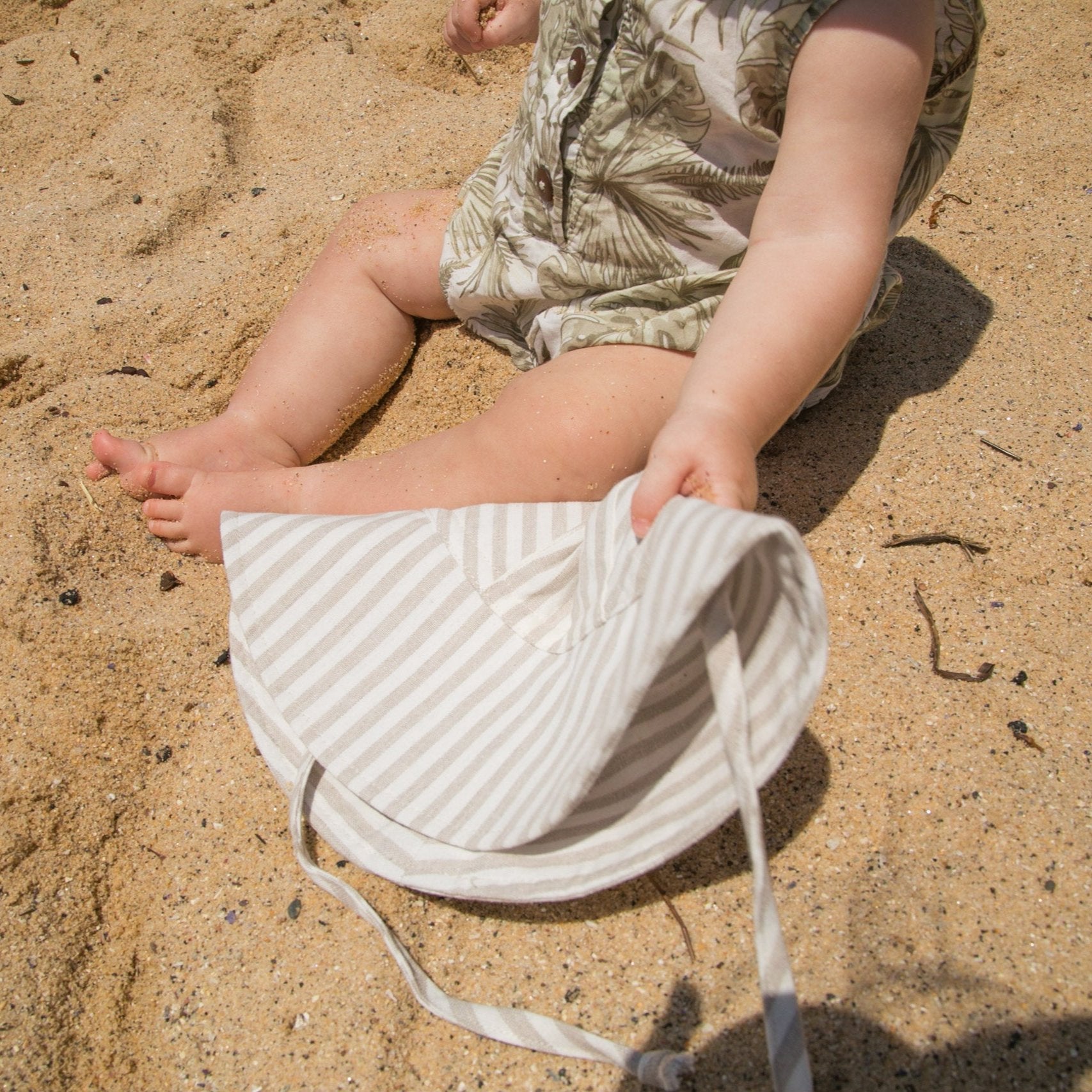 Lifestyle shot of Cloudy Stripes grey stripe baby sun hat, held by a baby enjoying the outdoors on a sunny day, highlighting its comfort and style