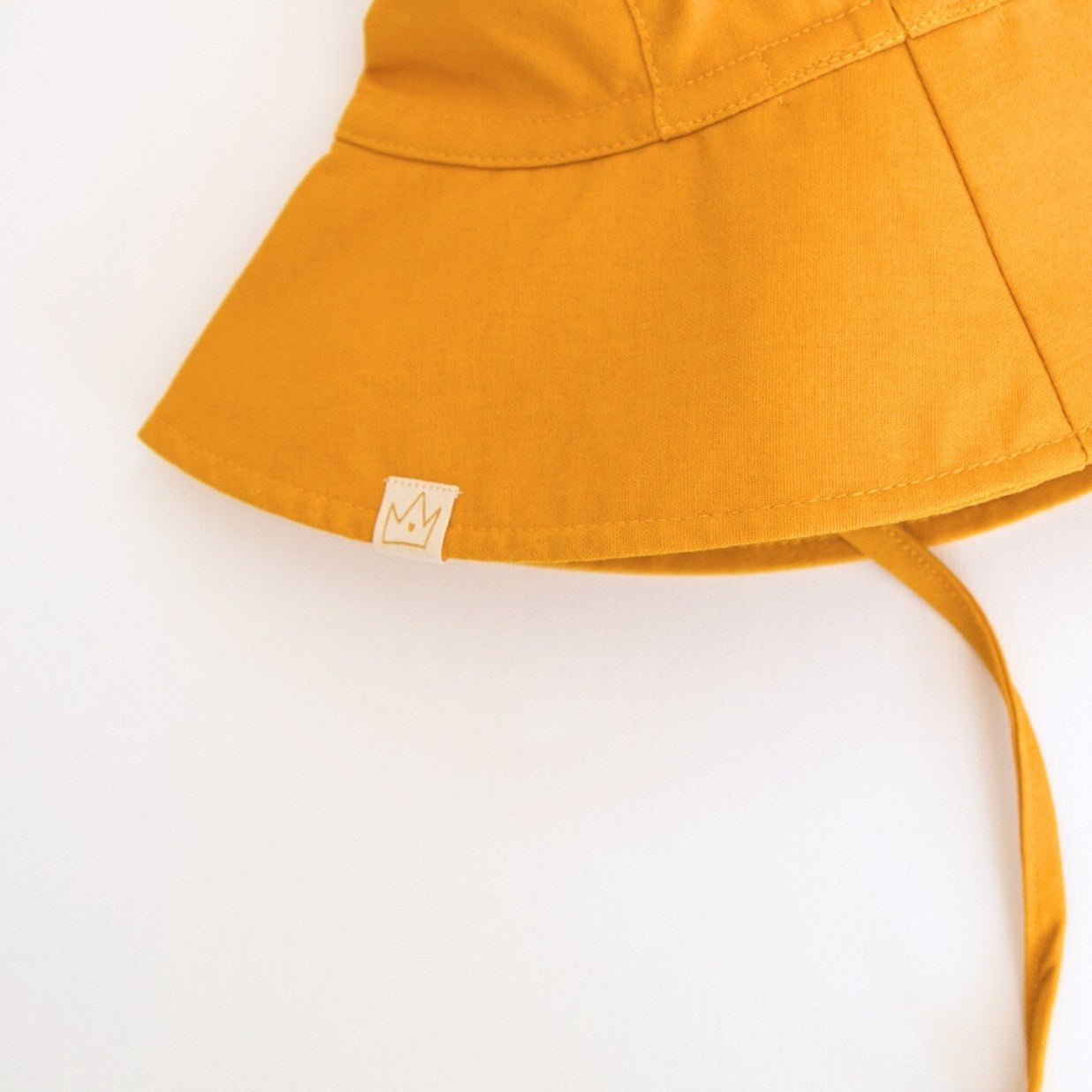 Back view of Golden Glow mustard baby sun hat, highlighting the adjustable neck tie for a secure fit and the exterior brand tag