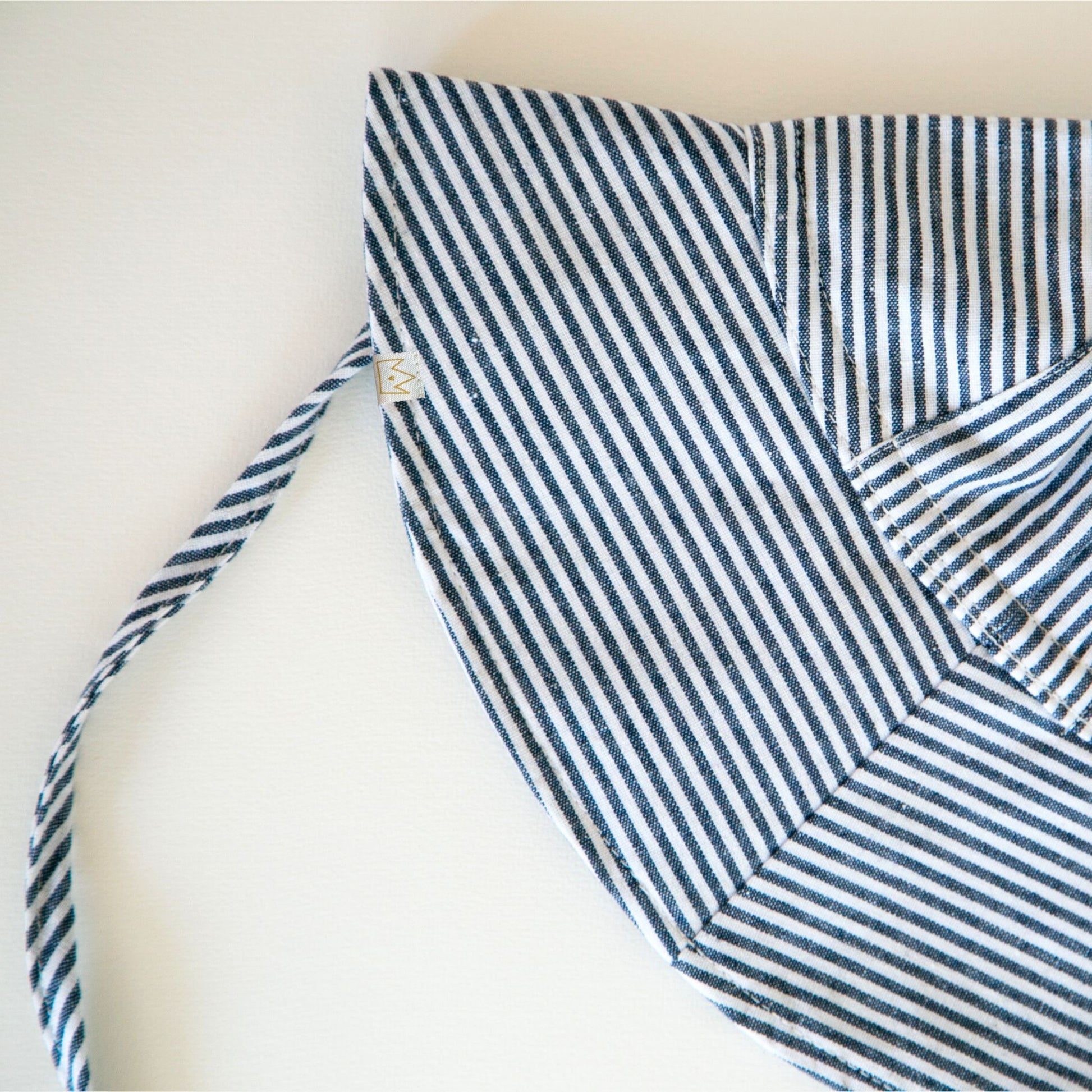 Back view of Ocean Breeze blue striped baby hat showing adjustable neck tie and soft breathable cotton as well as exterior brand tag