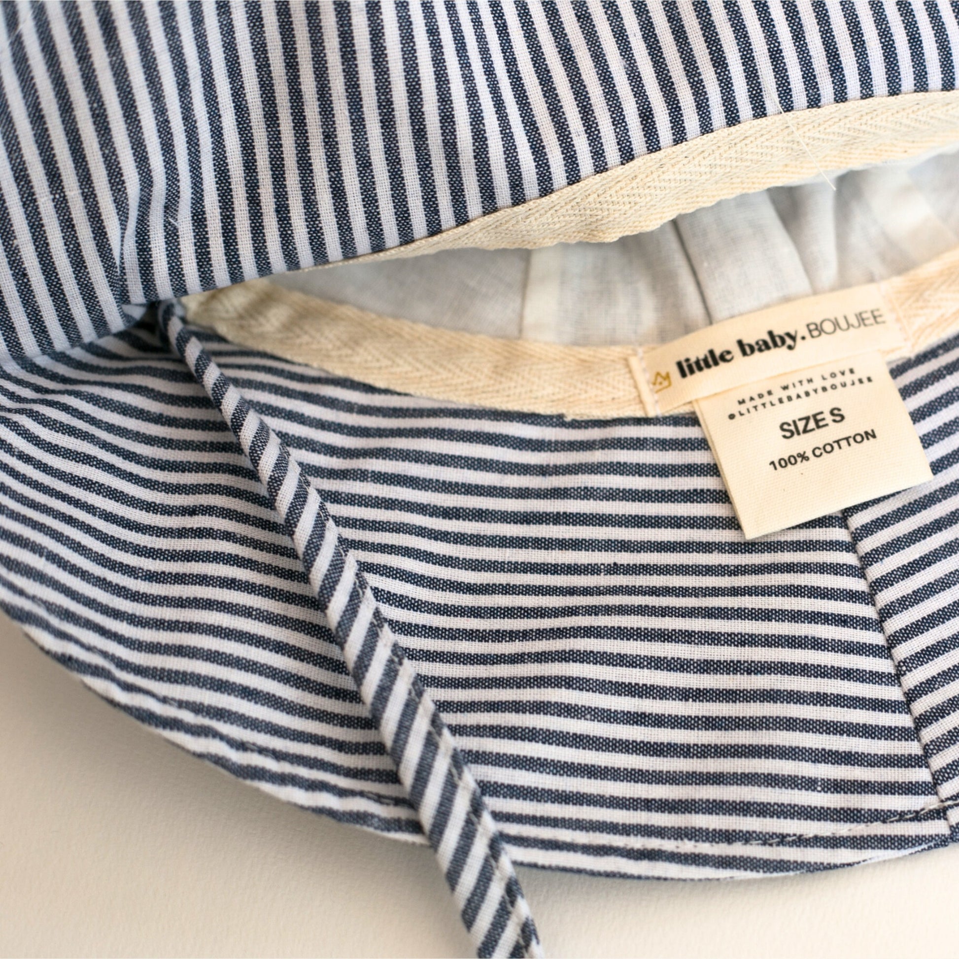Close-up detail shot of Ocean Breeze blue stripe baby sun hat, emphasising the breathable cotton material, stitching, and brand labels