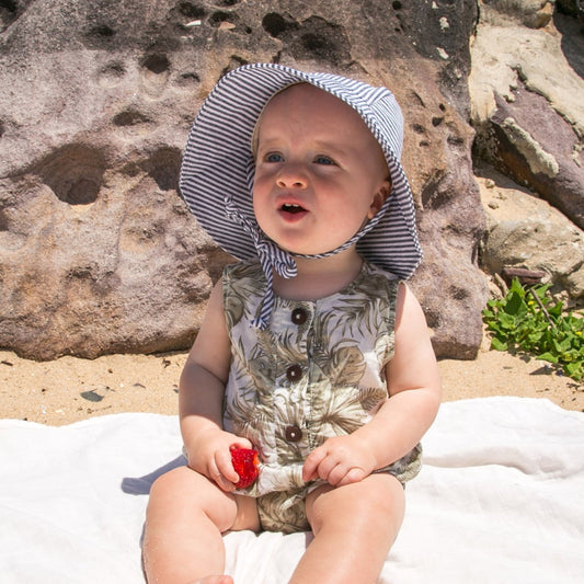 Lifestyle image of a baby wearing the Ocean Breeze blue stripe baby sun hat, enjoying the outdoors in breathable cotton comfort