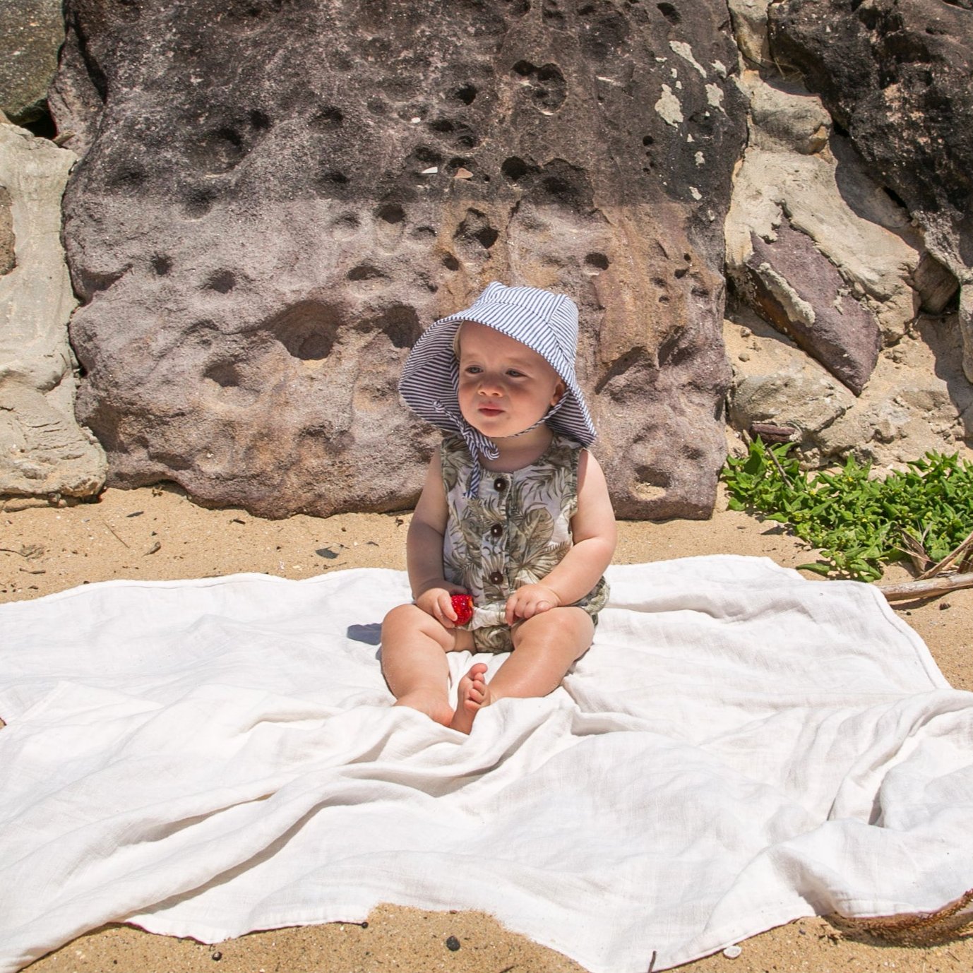 Lifestyle image of a baby wearing the Ocean Breeze blue stripe baby sun hat, enjoying the outdoors in breathable cotton comfort