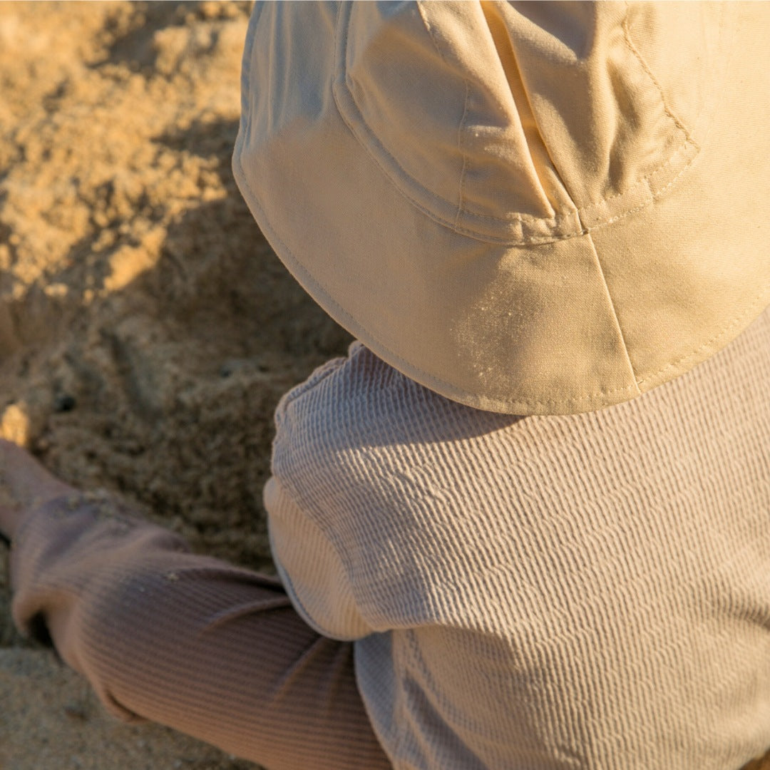 Baby wearing Sand Dune beige baby sun hat, made from breathable cotton with a wide brim for all-day comfort and style