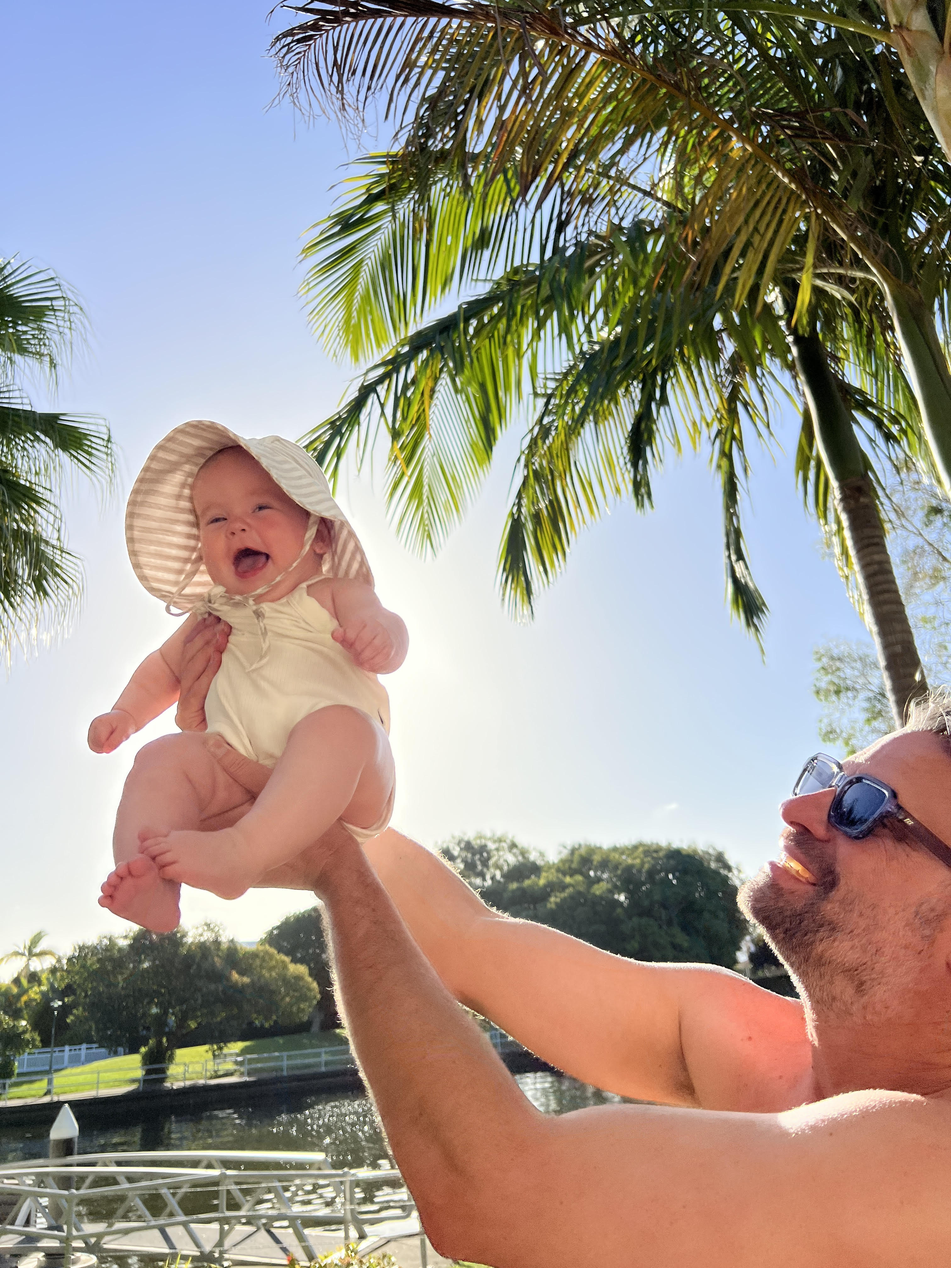 MAN HOLDING A BABY WEARING A HAT IN THE SUNSHINE ON HOLIDAYS